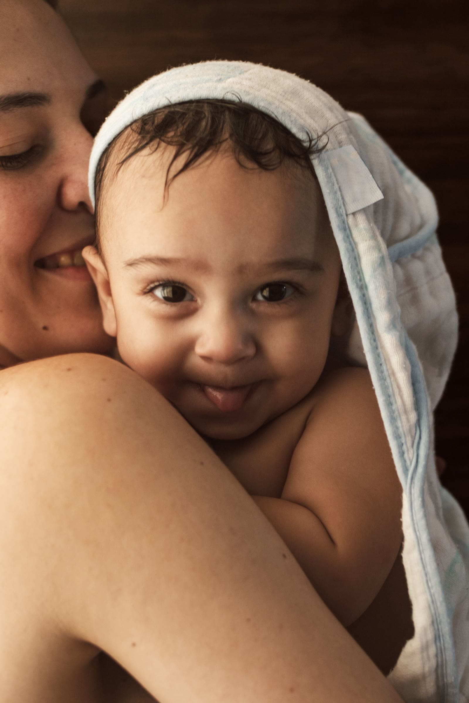 Una madre tiene in braccio il figlio avvolto in un asciugamano, nella luce del sole